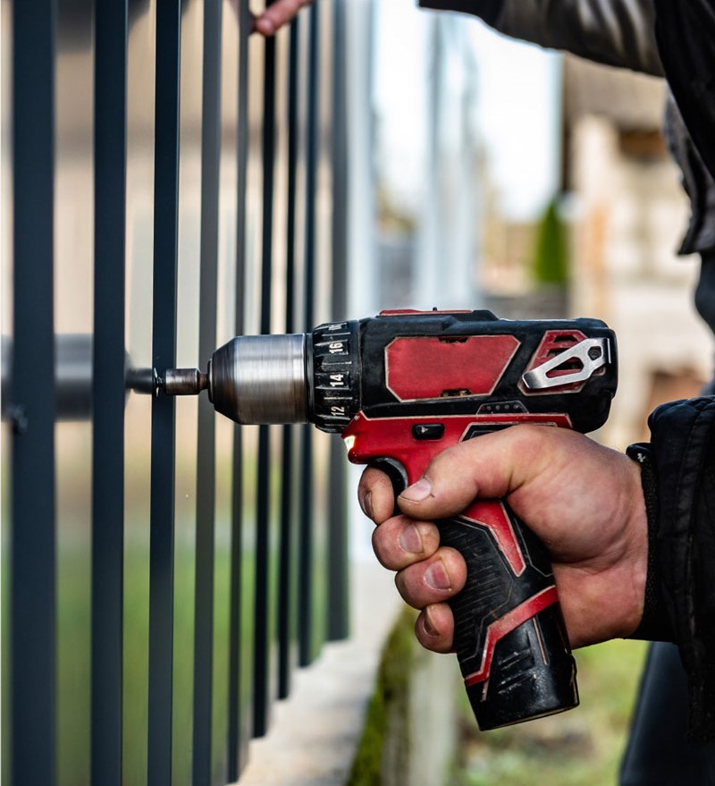 a man's hand using a power tool to install a black metal fence